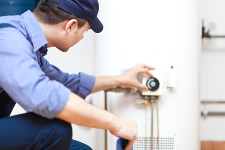 A worker in blue shirt and cap is adjusting a water heater.