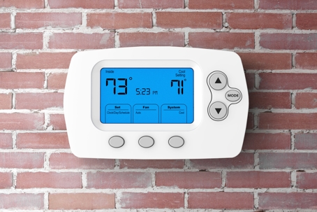 A white digital thermostat is mounted on a brick wall.