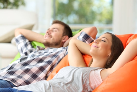 Two people are relaxing in orange beanbag chairs. They are wearing casual clothes.