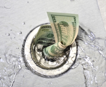 A twenty dollar bill is going down a drain. Water is splashing around it.