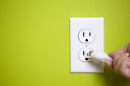 A white electrical outlet with a plug being inserted. Green wall.