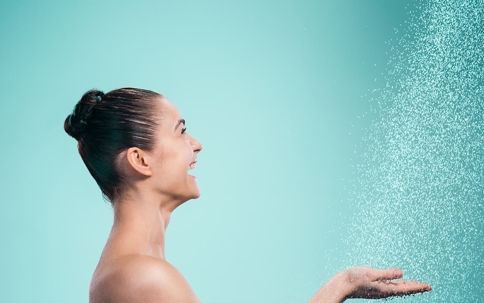 A woman smiling, is under a shower. Water droplets are falling.