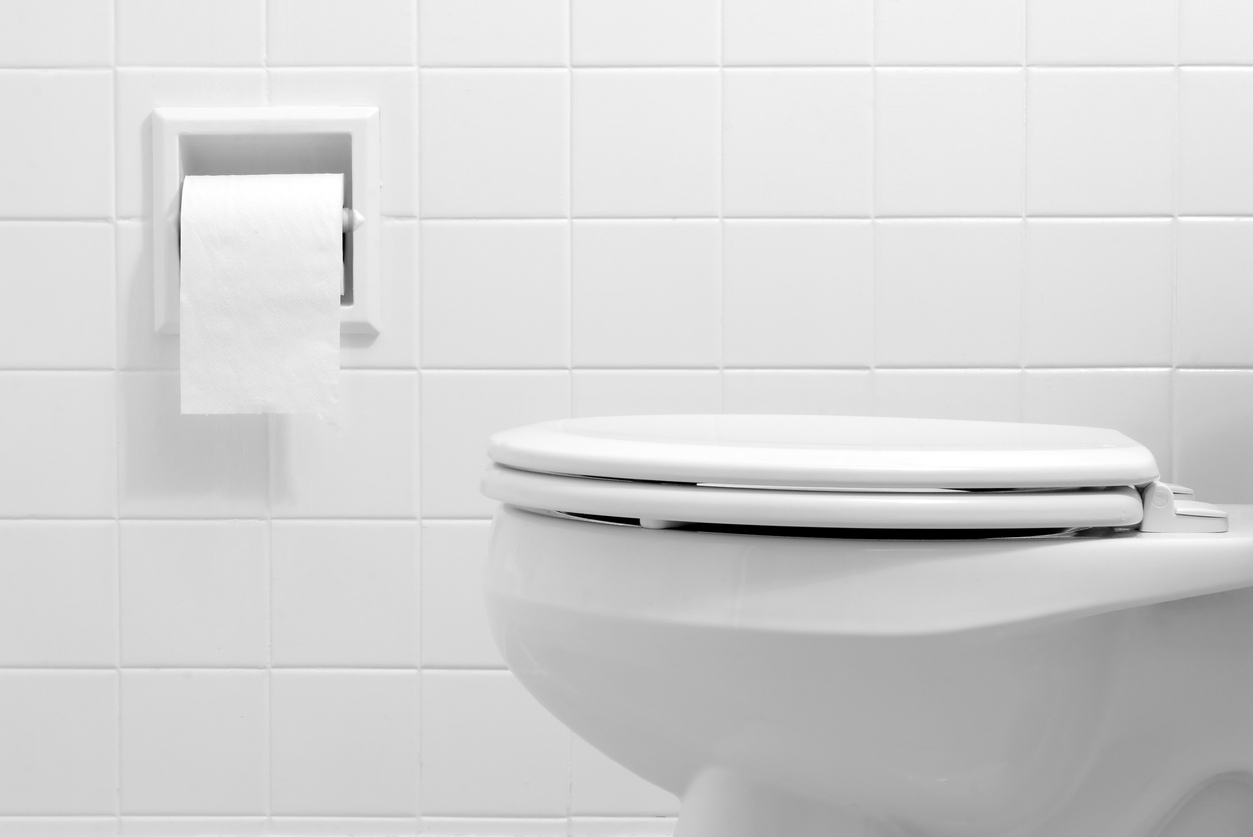 A white toilet with a closed lid and a paper towel dispenser on the wall.