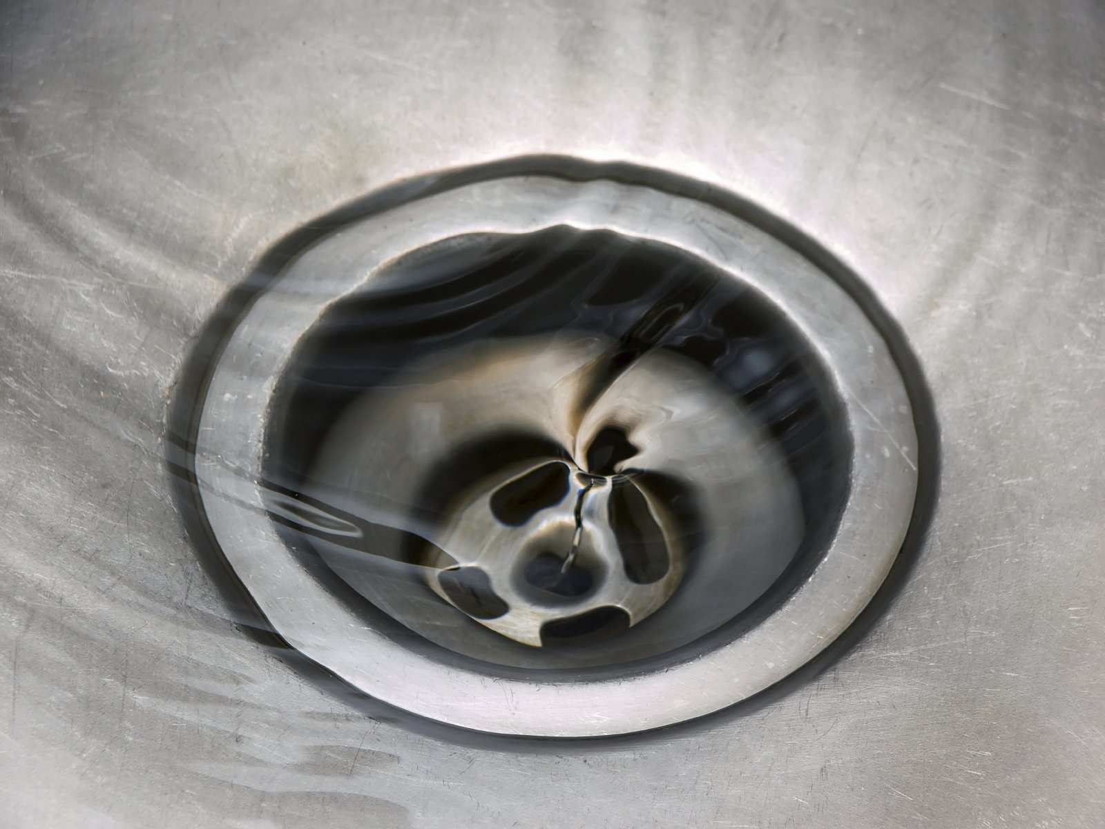 A gray metal sink drain with swirling water going down.