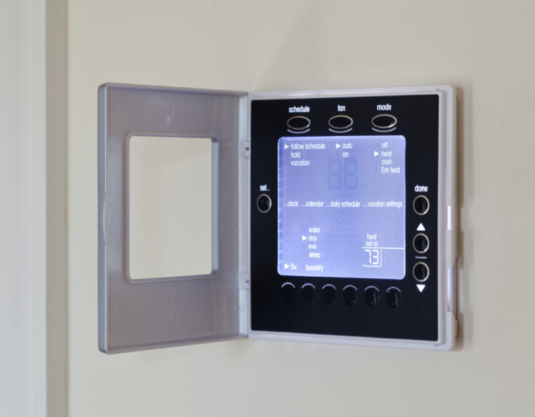 A digital thermostat with a display showing the temperature, schedule options, and fan/mode settings.