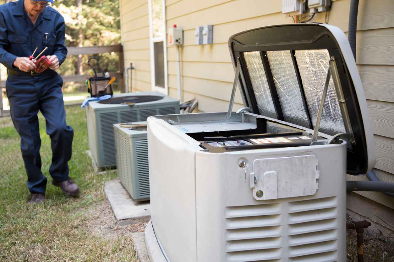 A generator box with its lid open, next to air conditioning units. A man is working nearby.